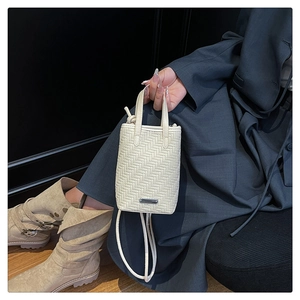 Detailed view of cream woven crossbody bag texture with silver plaque and shoulder strap