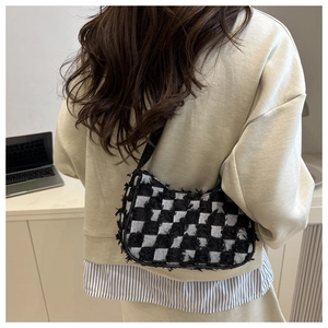 Detail of checkered denim bag with frayed edges worn by a model in an office setting