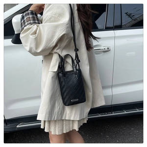 Detail of black woven crossbody bag featuring a herringbone texture and knotted shoulder strap