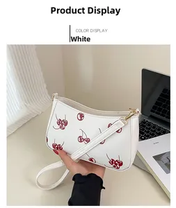 Close-up of white leather crossbody bag with cherry prints and gold hardware detail