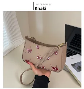Detail of khaki shoulder bag with red cherry print and golden zipper closure
