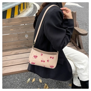 Sac bandoulière beige à motifs cerises porté par un mannequin assis sur un banc