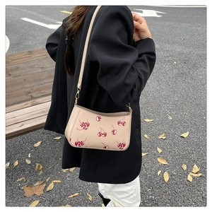 Detail of beige underarm bag with red cherry prints and gold hardware on model