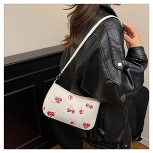 Gros plan du sac blanc à motif cerise porté sur une veste en cuir noir élégante