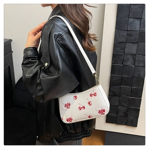 Close-up of white shoulder bag featuring red cherry prints and golden metal hooks