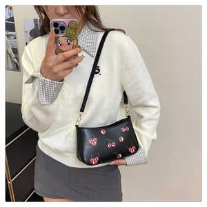 Détail du sac à bandoulière noir à motif cerise avec boucle dorée et longue lanière