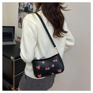 Gros plan d'un sac porté épaule noir à imprimé cerises avec boucle dorée sur la bandoulière