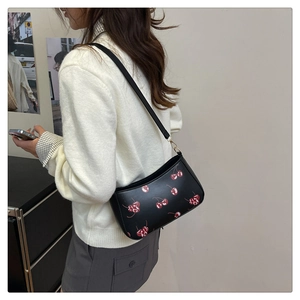 Détail d'un sac hobo avec imprimé cerise sur cuir noir porté à l'épaule par un mannequin