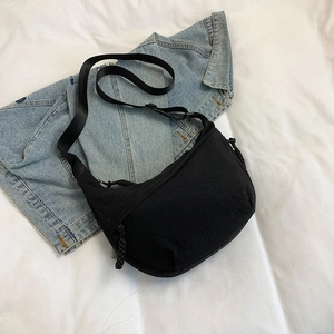 Minimalist black nylon crescent bag with adjustable strap on a denim jacket background