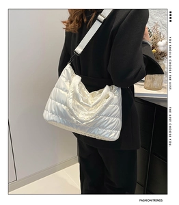 Side view of white quilted down shoulder bag with wide strap on a black blazer