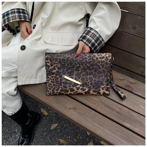 Detail of leopard print clutch with gold metal trim held by model on a bench