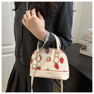 Détail du sac coquillage à motif fraises avec ferrures dorées et bandoulière blanche