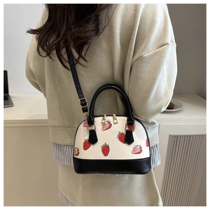 Detail of strawberry print shell bag worn as crossbody in a minimalist office setting