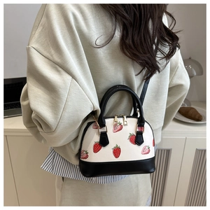 Detail of strawberry print shell bag featuring dual zippers and golden hardware