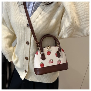 Detail of strawberry print shell bag with brown contrast handles and adjustable strap