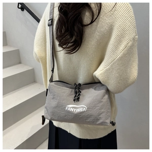 Gray crossbody bag with FANYISSA logo shown on model in a minimalist outdoor setting