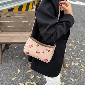 Petit sac bandoulière beige imprimé cerises avec boucle dorée porté par un modèle