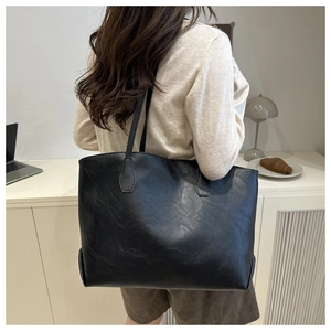 Detail of a large black matte tote bag worn on shoulder in an office workplace setting