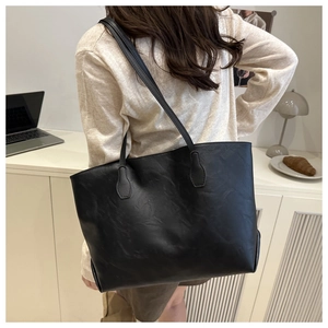 Large black leather tote bag worn by model in a cozy home office setting