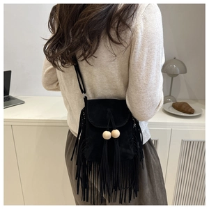 Detail of bohemian black suede crossbody bag with fringe tassels on a minimalist desk