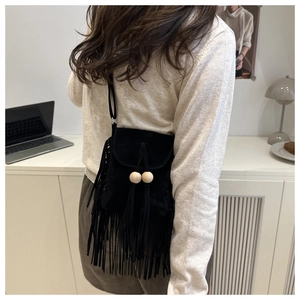 Detail of a black suede crossbody bag with fringe tassels and wooden bead accents