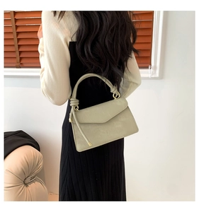 Sage green crossbody bag showing knotted handle and gold metal rings on a model