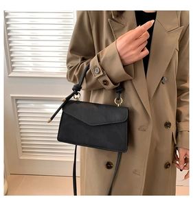 Detail of black crossbody bag with rope knot handle and gold hardware on trench coat