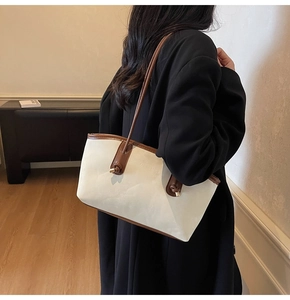 Close-up of a vintage beige tote bag with brown leather handles worn by a model