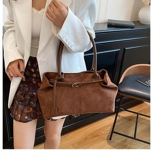 Detail of a brown suede tote bag with a long leather buckle strap on the soft folded front