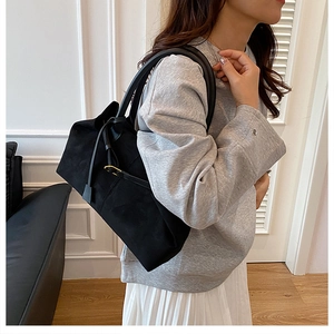 Detailed view of black suede tote bag with round leather handles and decorative tassel