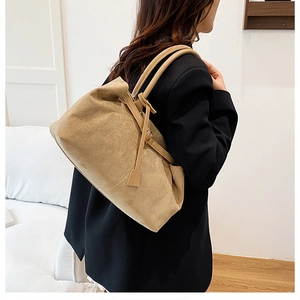 Close-up of khaki suede tote bag with dual straps worn over a black blazer