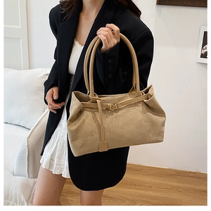 Detail of beige suede tote bag with long handles and decorative buckle in a home setting