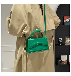 Bright green crossbody bag with wavy stitching worn over a stylish khaki trench coat