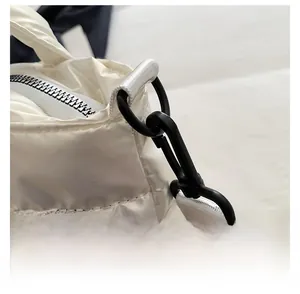 Detail of detachable black swivel hook and metal zipper on white quilted puffer tote bag