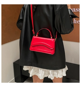 Detail of red glossy square bag featuring wavy flap design and gold metal hardware