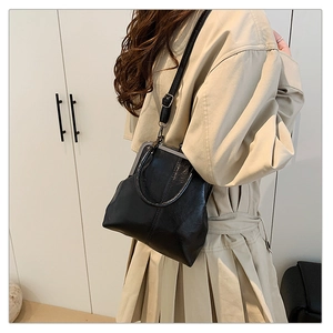 Retro doctor bag with metal clasp and thin leather strap shown on beige trench coat