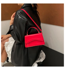 Detail of bright red crossbody bag with wavy flap design and gold hardware on model