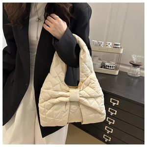 Detail of quilted tote bag with large bow decoration held by model in lifestyle setting