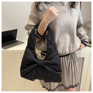 Close-up of quilted black bag featuring a decorative large bow and diamond stitch texture
