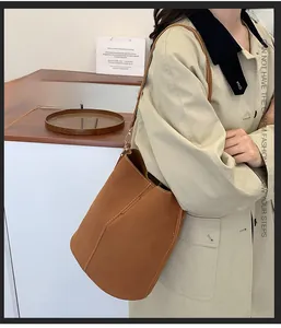 Detail of a caramel matte leather bucket bag with slim shoulder strap worn by a model