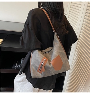 Detail of a grey canvas hobo bag with brown leather straps shown on a model's shoulder
