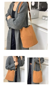 Detail of a brown bucket bag showing contrast stitching and wide woven shoulder strap