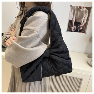 Side view of black quilted shoulder bag featuring a large decorative bow and rhombic texture