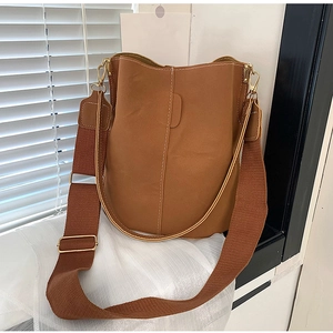 Detail of caramel leather bucket bag with wide fabric strap and contrast stitching accents