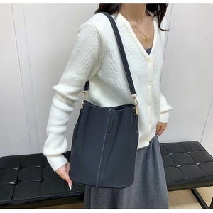 Detail of dark gray bucket bag featuring white contrast stitching and gold metal hardware