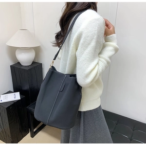 Detail of minimalist black bucket bag with white stitching and gold hardware on model