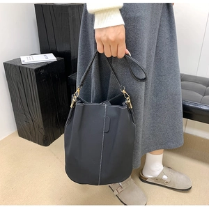 Detail of black bucket bag featuring white contrast stitching and gold metal hooks