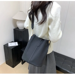 Detail of a black bucket bag with white contrast stitching and canvas shoulder strap