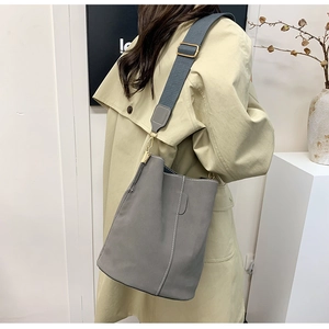 Detail of grey bucket bag with white stitching and wide fabric strap on a beige coat