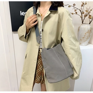 Detail view of a gray bucket bag featuring wide woven strap and contrast white stitching